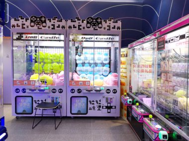 Çin, Shenzhen - 25 Ekim 2024: İçinde pelüş oyuncaklar olan iki pençe makinesi modern bir alışveriş merkezinde cam önlü bir atari oyununun yanında duruyor.