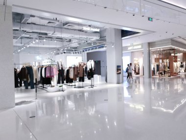 Çin, Shenzhen - 25 Ekim 2024: Beyaz duvarlı ve zeminli modern bir alışveriş merkezi, mankenler sergilenen giyim mağazaları.