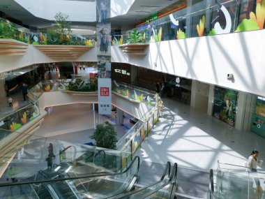 Çin, Shenzhen - 25 Ekim 2024: Yürüyen merdivenleri, büyük pencereleri ve saksı bitkileri olan modern bir alışveriş merkezinin üst katlarından bir manzara.