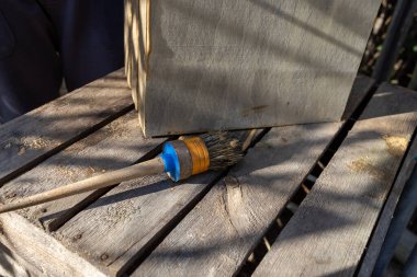 Bir çocuk, bahçesinde fırça olan ahşap bir kutu boyuyor.