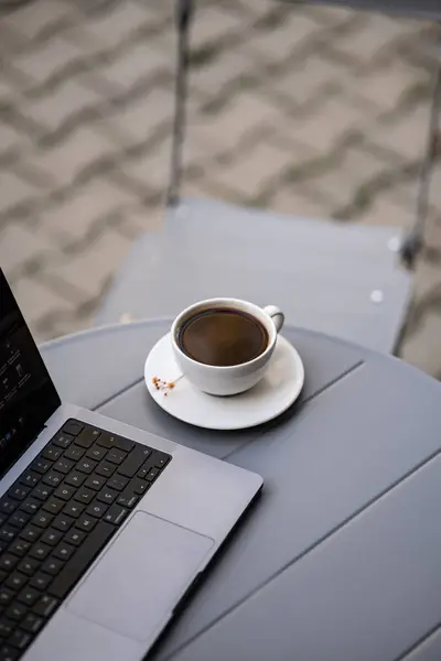 a laptop with a cup of cappuccino coffee and a notebook on the table