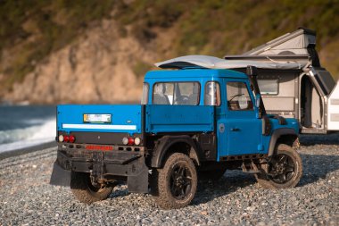 Deniz kıyısında karavanı olan mavi bir cip..