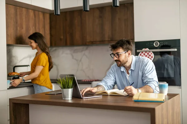 Genç adam dizüstü bilgisayarla uğraşırken mutfakta oturuyor. Evde dizüstü bilgisayarla çalışan genç bir serbest yazar..