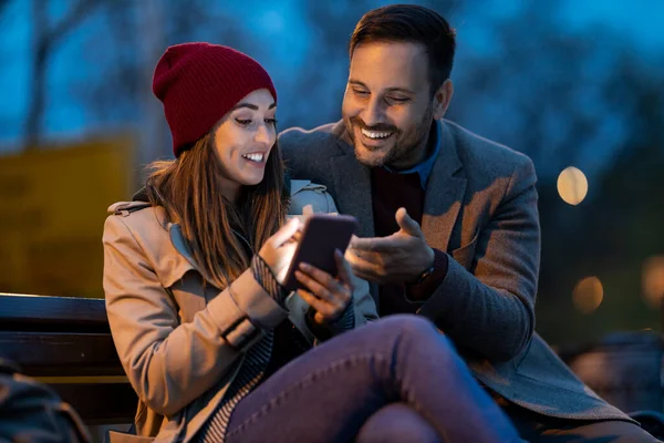 Glada Unga Par Sitter Parkbänk Och Använder Smarttelefon Njuter Natten — Stockfoto
