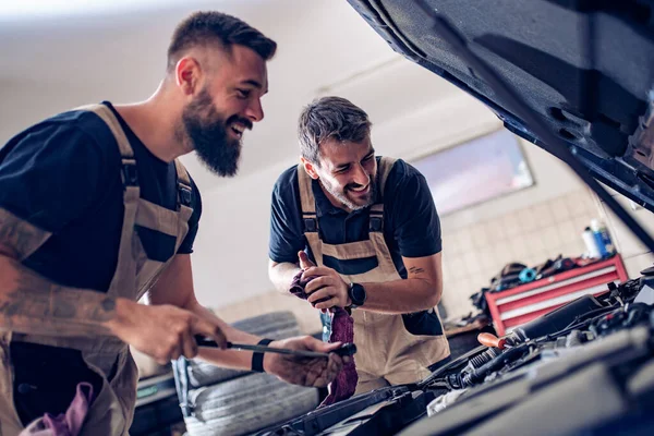 Young auto mechanics repairer change old motor oil and pour new oil into the car engine tank in vehicle workshop.