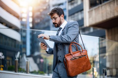 Checking statistics. Confident businessman standing and checking news on the tablet in front of business center.