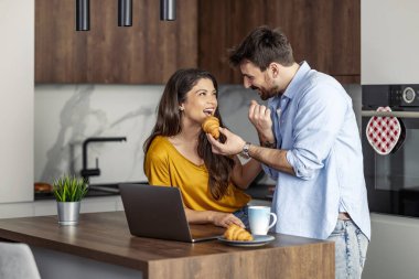 Mutfakta kahve içerken dizüstü bilgisayar kullanan çift. Modern mutfakta dizüstü bilgisayar kullanan çift..