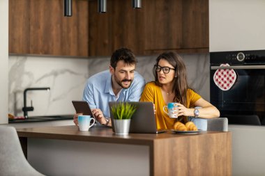Evde otururken, kadın ve erkeğin birlikte kahve içip dizüstü bilgisayarda çalışması..