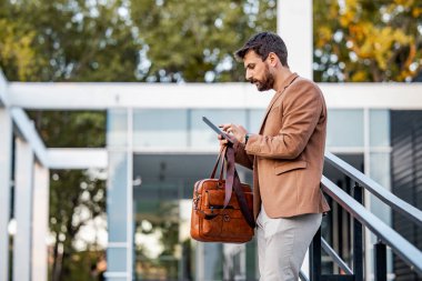 Modern binanın önünde dikilirken dijital tablet kullanan işadamının portresi.