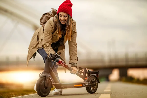Young woman is ready to discover the city in autumn at sunset with electric scooter. Electric transportation concept.