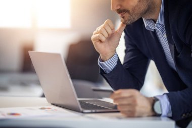 Parlak, modern bir ofis ortamında, üretkenlik ve konsantrasyon sağlayan bir dizüstü bilgisayar üzerinde çalışan bir iş adamı..
