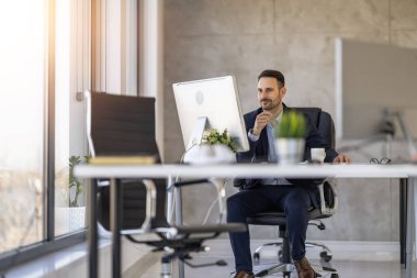 Modern ofis ortamında profesyonel bir işadamı masasında dikkatle çalışıyor. Görüntü profesyonelliği, konsantrasyonu ve çağdaş çalışma ortamını aktarır..