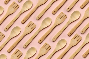 Tekrarlanan ahşap kaşık ve çatal pembe arka planda.