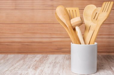 Kavanozun içindeki ahşap mutfak aletleri, kaşık, çatal, kurutucu ve maşalar, dekoratif olarak ahşap arka planda düzenlenmiş..