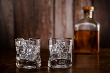 Buzlu iki boş viski bardağı. Arka planda çözülmüş viski şişesi var..