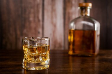 Buzlu bir bardak viski, arka planda odak dışı viski olan bir şişe..