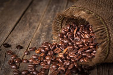 Kahve çekirdeği çuvalı eski bir kırsal masada devrildi. Fasulyeler tepesine saçıldı..