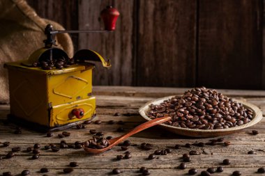 Roasted coffee beans on a plate and in a wooden spoon next to an old-fashioned grinder for grinding coffee. clipart