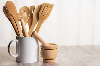 Bir kavanozun içindeki kaşıklar, çatallar ve maşalar gibi ahşap mutfak aletleri ve ahşap tezgahın yanındaki havan topu..