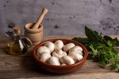 Çamurlu bir kabın içinde çiğ mantar, havan topu ve bazı baharat bitkilerinin yanında.. 