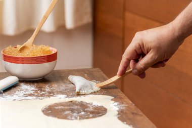 Man's hand with a wooden fork closing the puff pastry filled with angel hair or pumpkin candy.