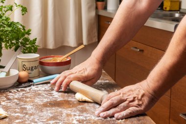 Man's hands with a rolling pin preparing a puff pastry dough in a home kitchen.