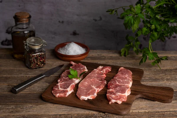 Iberian pork loin steaks on a cutting board, on a rustic old wooden table with olive oil, peppercorns and coarse salt.