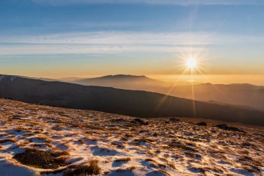 Landscape on the south face of the Sierra Nevada at sunrise, hill with plants and snow and the sun rising in the background over the mountains.Granada.