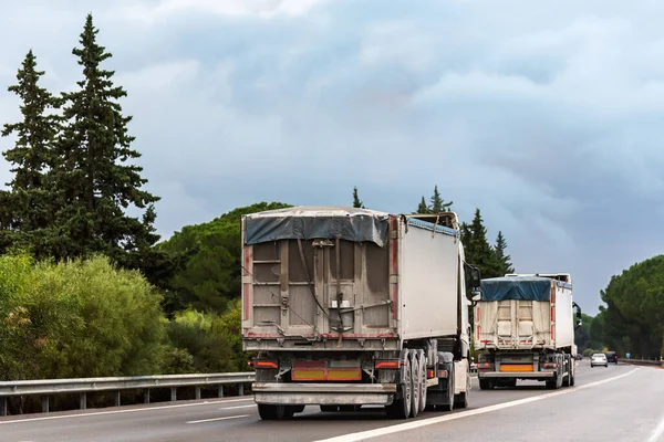 Trucks with tarpaulin tippers for bulk transport driving on a highway.