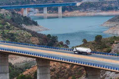 Tanker truck with dangerous goods plates driving through a viaduct over a swamp. clipart