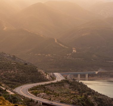 Güneşin doğuşuyla birlikte yüksek dağlar, bir bataklık ve etrafı köprülerle çevrili bir otoyol. Pantano de Rules..