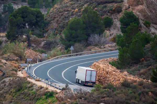 Truck with a refrigerated semi-trailer driving on a two-way road, with two uphill lanes, one for slow vehicles.