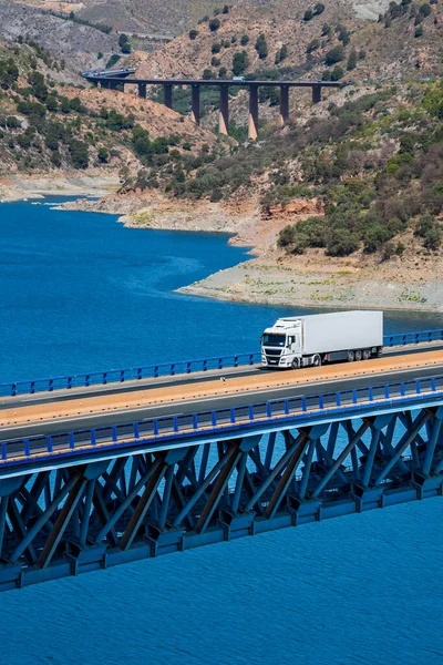 Truck with a refrigerated trailer driving on a metal bridge.