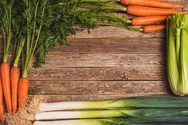 Yeşil saplı, pırasalı ve kerevizli havuçlu eski ahşap tahtaların arka planı.