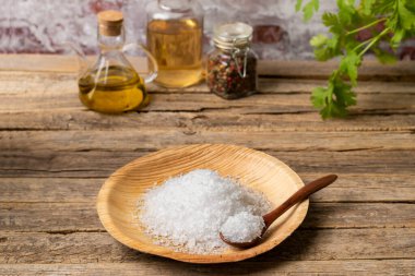 Tuz taneli ahşap tabak, kırsal ahşap masa üzerinde biber, sirke ve zeytinyağı kavanozları ile.