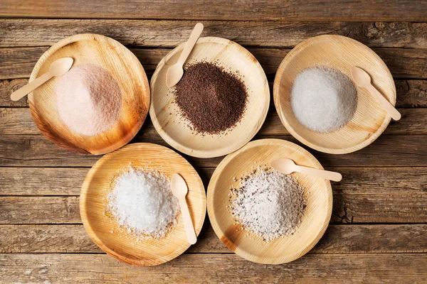 stock image Wooden plates with different types of salt, pink, black, marine or normal, flakes and seasoned with truffle, on a rustic wooden table. 