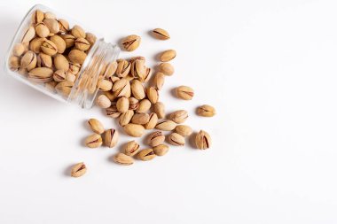 Cam kavanoz, beyaz arka planda, fındıklardan dökülen şam fıstıklarıyla yatıyordu..