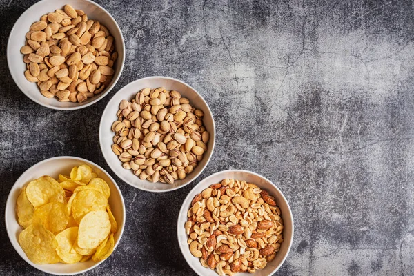 Bowls with chips and nuts, almonds, pistachios and a mix of peanuts, cashews, hazelnuts and roasted almonds.