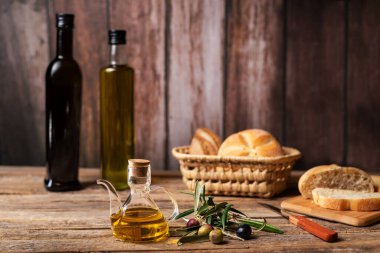 Zeytin dalının yanında zeytin yağı ile yağlı sürahi, arka planda ekmek ve birkaç şişe zeytinyağı..