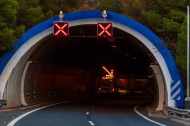 Otoyoldaki bir tünel, içinde hafif bir ok bulunan, içinde bakım aracı bulunan kapalı şeritler için uyarı işareti olan bir tünel..
