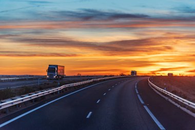 Ufukta gün batımında bir otoyolda giden kamyonlar geceye yol vererek nefes kesici manzaralar altında iş talep ediyor..