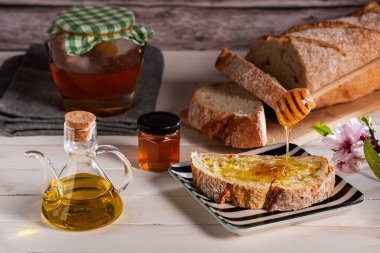 Zeytin yağı ve bal ile kızartılmış ekmek, beyaz bir masanın üzerinde bir kavanoz bal ve dilimlenmiş bir somun ekmek..