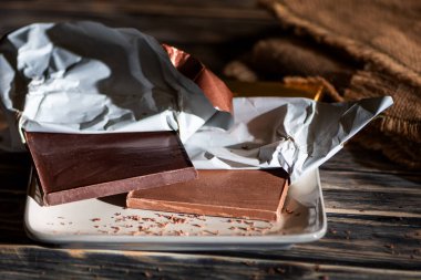 Koyu ve sütlü çikolatalar tabakta, sanatsal çikolatalar, ahşap bir masanın üzerinde, kırsal bir arka planı var..