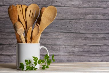 Beyaz seramik sürahi ahşap mutfak gereçleriyle dolu. Köy arka planında taze maydanozun yanında.. 