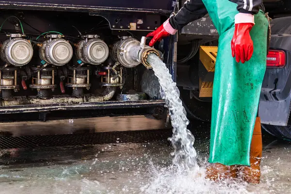Tanker kamyon yıkama istasyonunda çalışan, kapağı açık, iç yıkama işleminden sonra temizlik suyu boşaltan, uluslararası temizlik sertifikasını elde etmek için zorunlu temizlik yapan biri..