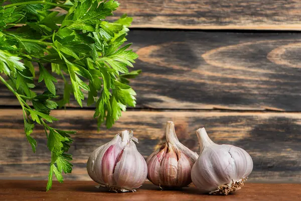 Sarımsak soğanları ahşap bir masada, bir tarafta maydanoz filizleri, eski koyu ahşap bir arka plan ve kopyalama alanı..