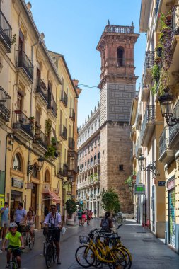 Valencia, İspanya - 12 Ağustos 2022: Güneşli bir yaz gününde Ortaçağ Serranos Kulesi 'nin altındaki dar Carrer de Serrans' da bisikletçiler ve yayalar dolaşır.