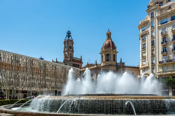 Valencia, İspanya - 12 Ağustos 2022: Süslü macenta kaplı belediye binası, hareketli Plaza del Ayuntamiento Meydanı 'ndaki dairesel bir fıskiyenin çağlayan su fıskiyeleri tarafından çerçevelenmiştir..