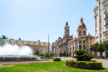 Valencia, İspanya - 12 Ağustos 2022: Süslü macenta kaplı belediye binası, hareketli Plaza del Ayuntamiento Meydanı 'ndaki dairesel bir fıskiyenin çağlayan su fıskiyeleri tarafından çerçevelenmiştir..