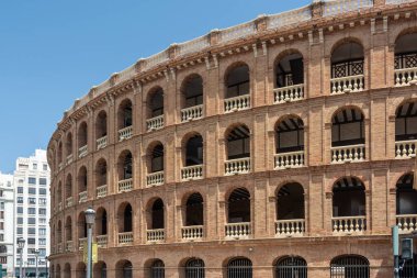 Valencia, İspanya - 12 Ağustos 2022 Plaza de Toros de Valencia 'nın kıvrımlı tuğla kemerlerinin yanından geçen yayalar, açık mavi gökyüzünün altındaki 19. yüzyıldan kalma bir bulvar taşı..